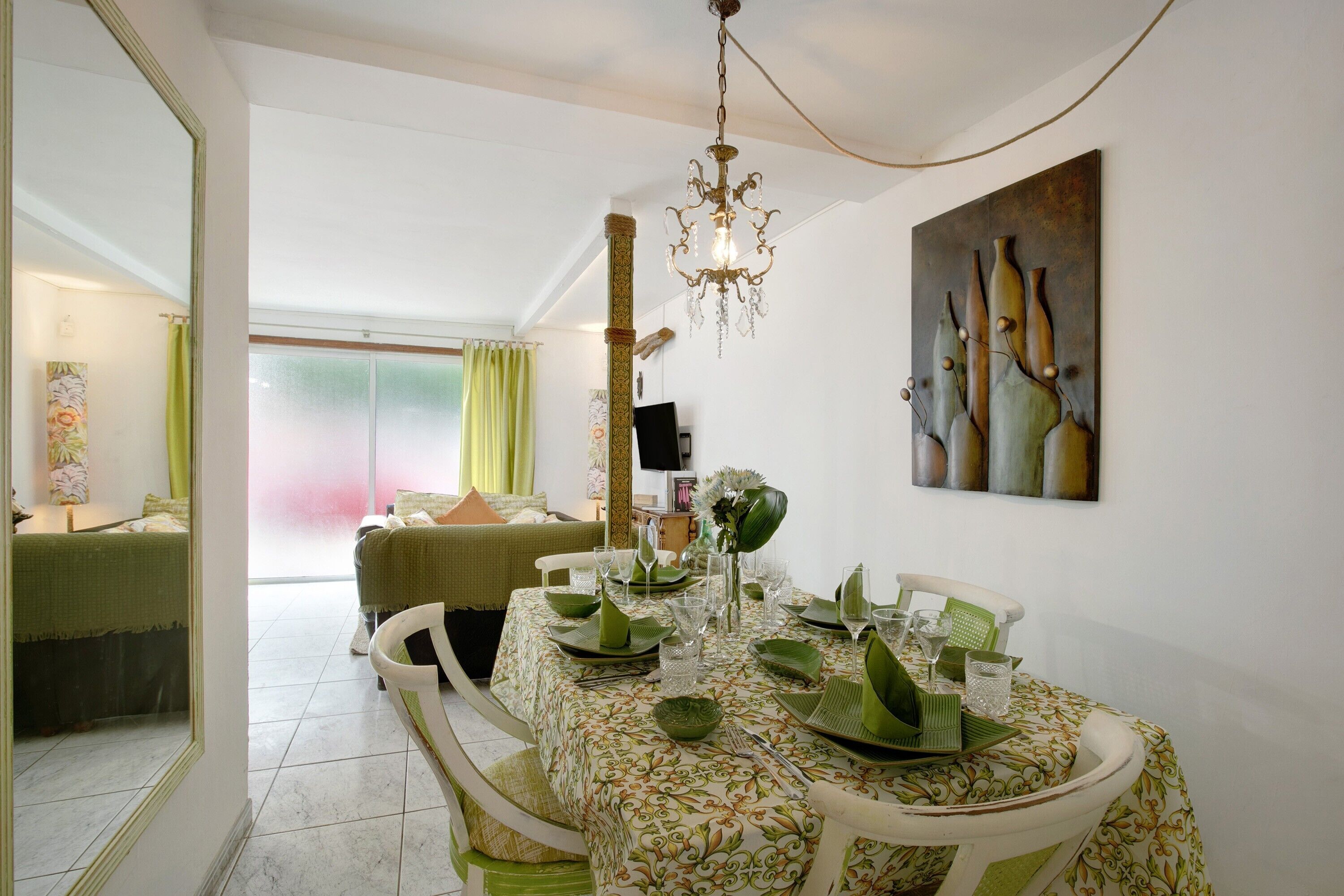 A dining area with a table set for four, a chandelier, and a painting on the wall.