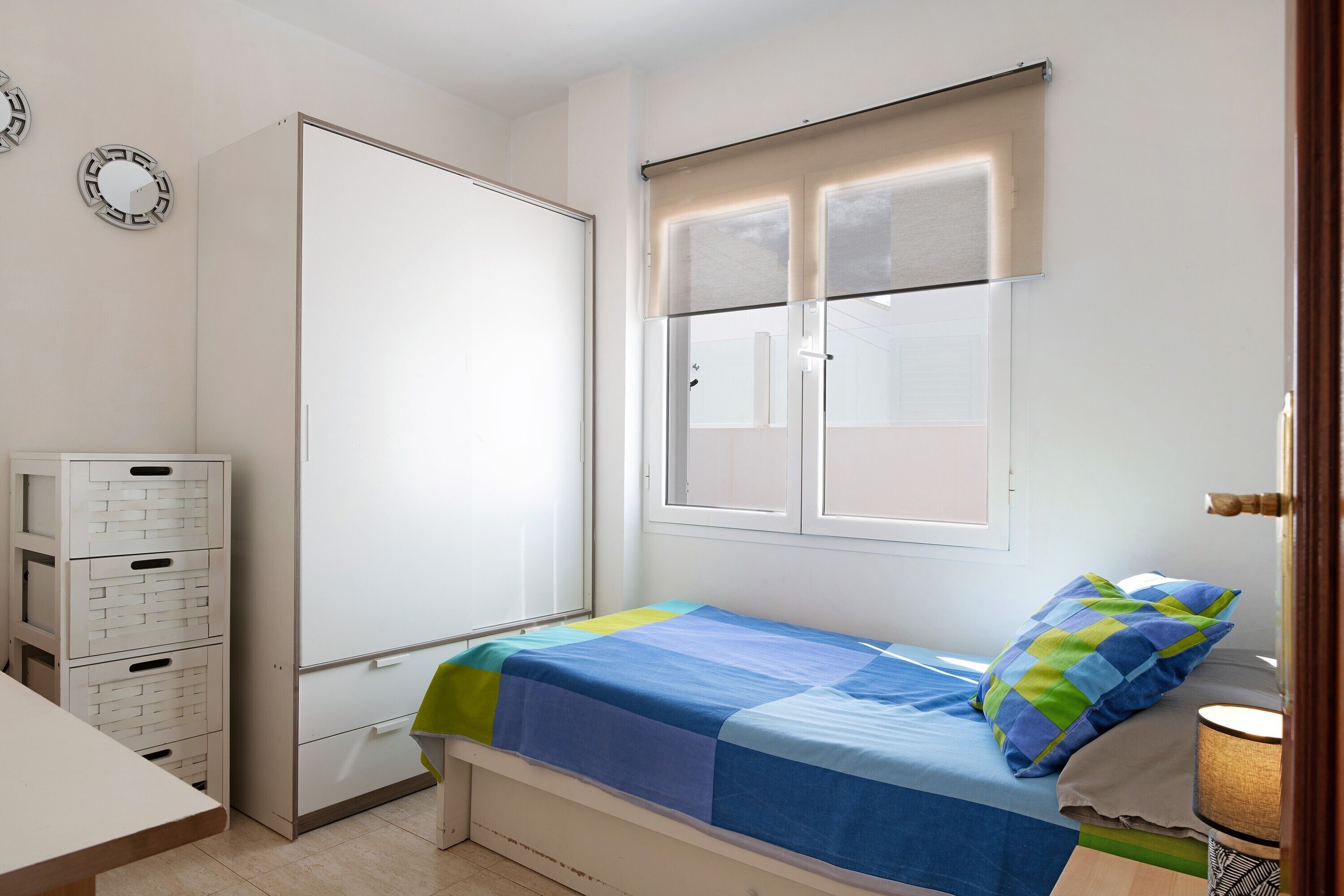 A bedroom with a bed, a window, a desk, and a wardrobe.