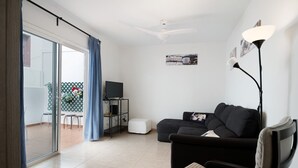 A living room with a sofa, a TV, a lamp, and a sliding glass door leading to an outdoor area. - Vacation Home "Casa Tipica Canaria" with Sea View, Private Terrace & Wi-Fi (Playa Honda)