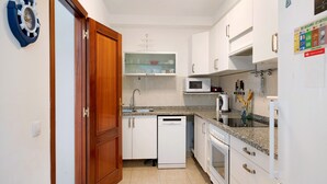 A compact kitchen with white cabinets, a microwave, a dishwasher, and a wooden door. - Vacation Home "Casa Tipica Canaria" with Sea View, Private Terrace & Wi-Fi (Playa Honda)