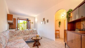 Una sala de estar con un sofá, una mesita con un florero, un aparador de madera y una ventana con vista a la vegetación.