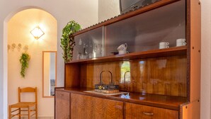 Un aparador de madera con puertas de cristal, una cesta de mimbre con flores y una silla.