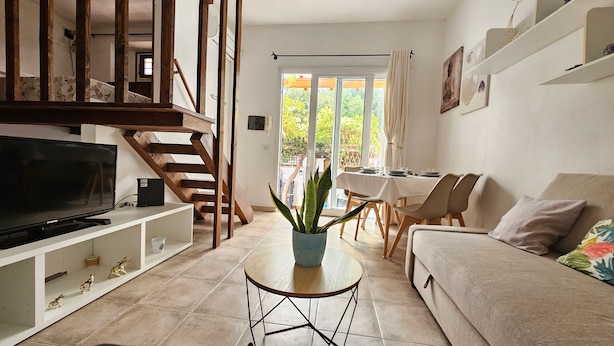 A living room with a TV, sofa, dining table, chairs, staircase, and a potted plant. - Apartment "In Casetta" with Private Garden and Wi-Fi (Cagliari)