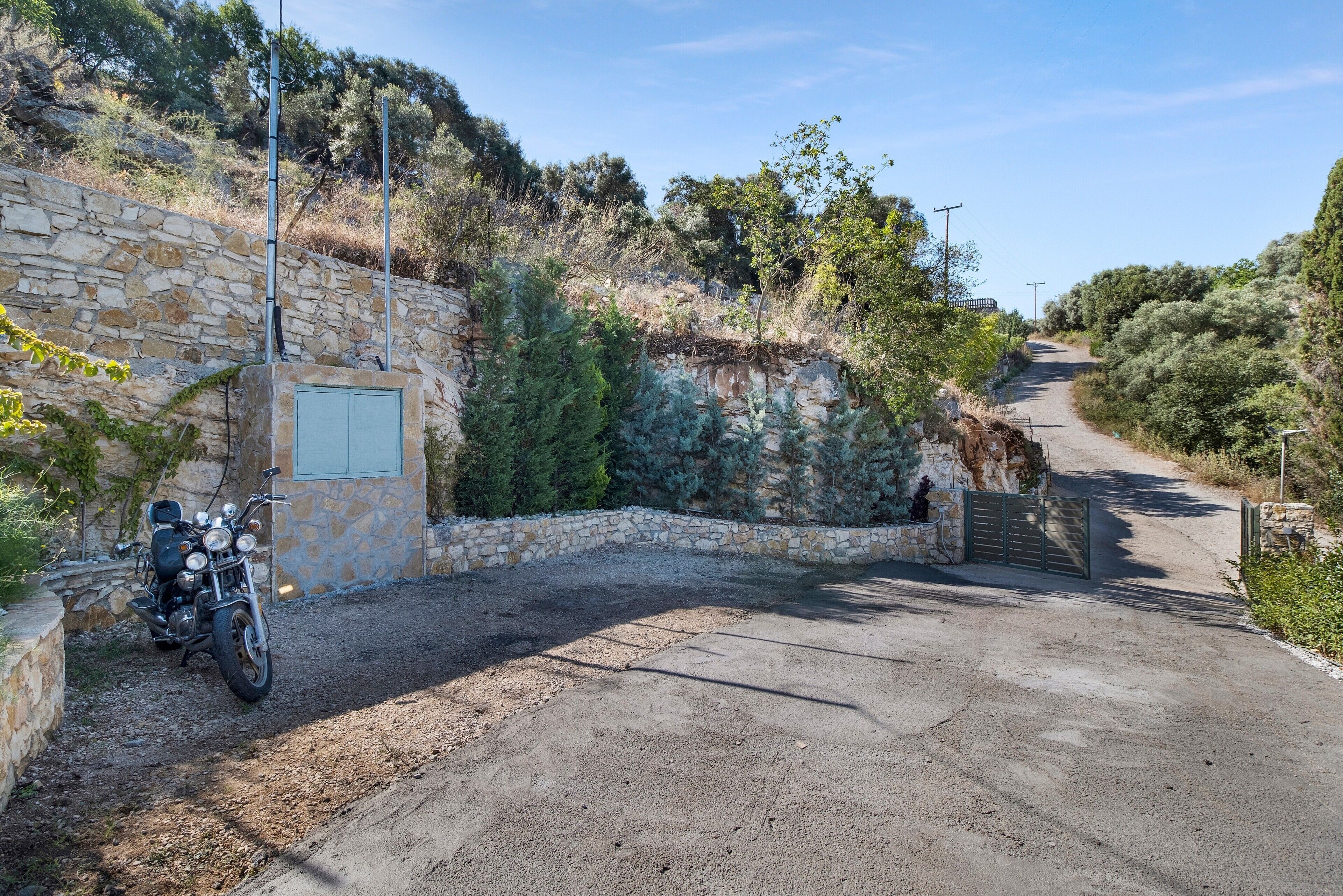 A paved driveway leading to a stone wall with a motorcycle parked on the left.
