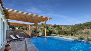 Una piscina con pérgola, sillas de descanso y un deck de piedra.