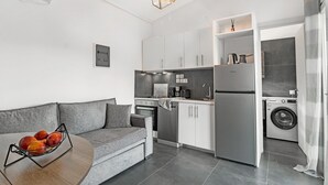 Una cocina moderna con electrodomésticos integrados, un sofá gris y un frutero sobre una mesa redonda.