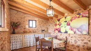 Un interior rústico de piedra con vigas de madera, una mesa de comedor con sillas, una zona de cocina y un mural temático de frutas.