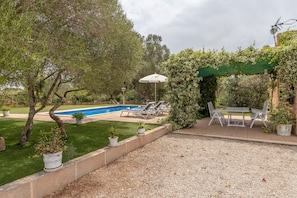 A pool area with lounge chairs, a table, and a pergola with climbing plants.