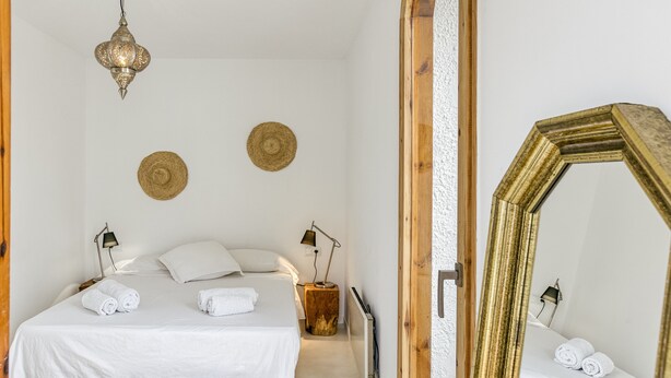 A bedroom with a bed, two bedside lamps, a hanging light fixture, two wall-mounted woven baskets, and a large mirror. - Holiday Home 'Villa La Barrufa' with Shared Pool, Private Terrace and Wi-Fi (S'Agaró)