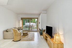 A modern living room with a sofa, a wicker chair, a television, and a wooden console. - Holiday Home 'Villa La Barrufa' with Shared Pool, Private Terrace and Wi-Fi (S'Agaró)