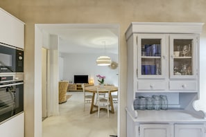 A kitchen with a Bosch oven, a dining area with a round table and chairs, and a cabinet with glass doors. - Holiday Home 'Villa La Barrufa' with Shared Pool, Private Terrace and Wi-Fi (S'Agaró)