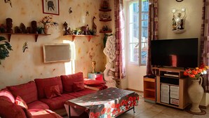 A living room with a red sofa, a coffee table with a floral tablecloth, a TV on a wooden stand, and various wall decorations. - Apartment 'Loft Americain Centre Ville' with Wi-Fi (Marseille)