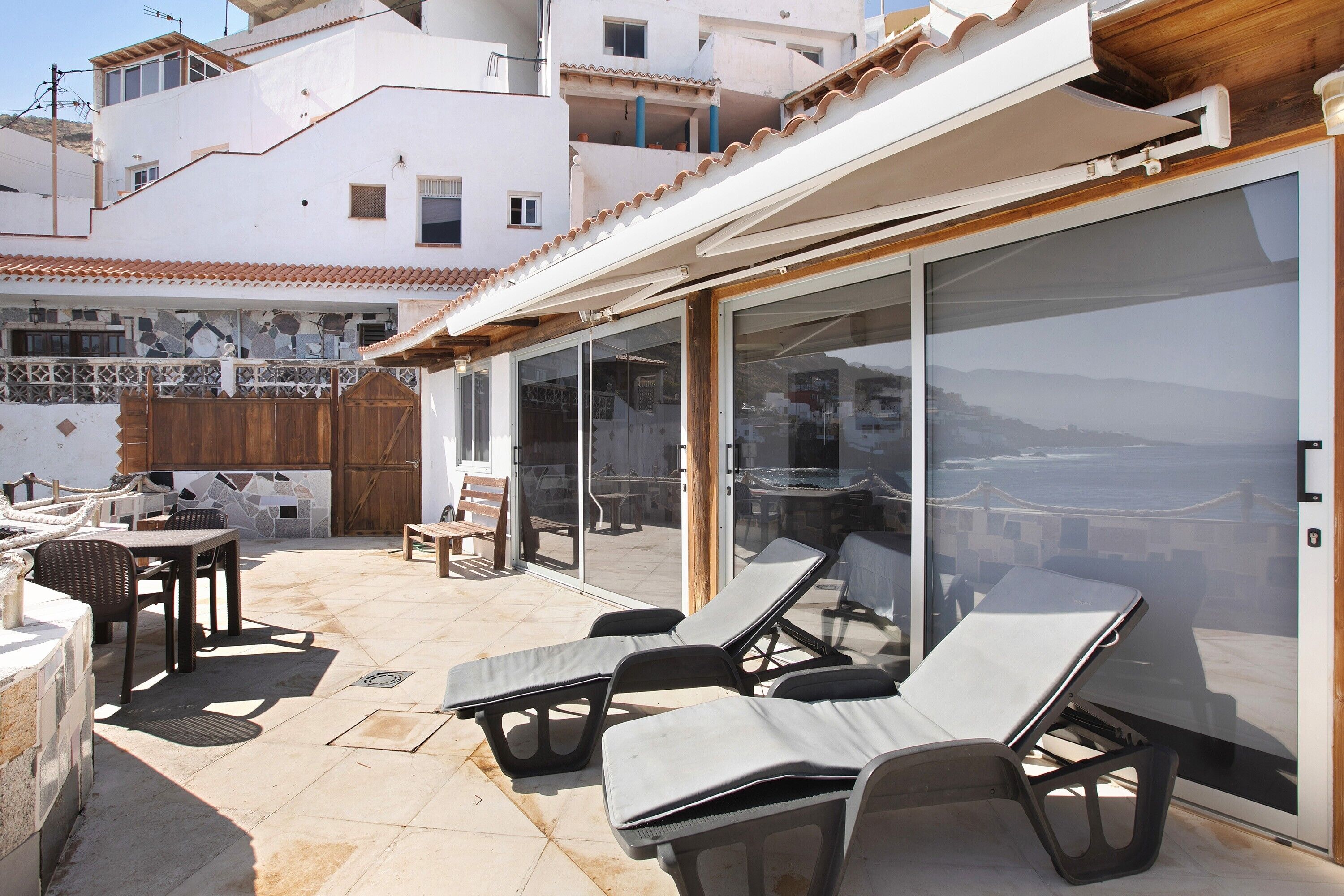 An outdoor patio with lounge chairs, a table, and a glass door leading to a balcony.