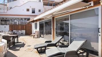 An outdoor patio with lounge chairs, a table, and a glass door leading to a balcony.