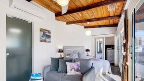 A bedroom with a bed, bedside lamps, a wooden ceiling, and a view through a glass door.