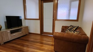 Un salón con un sofá de cuero marrón, un mueble de televisión de madera con una televisión de pantalla plana y un ventanal corredizo que da a un balcón.