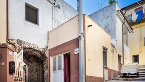 Eine enge Straße mit einem Gebäude, das ein steinernes Tor, eine weiße Tür und einen kleinen Balkon mit einer Matratze zeigt.
