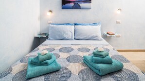 Ein Hotelzimmer mit einem Bett, zwei Kissen, einem Nachttisch, einem Wandbild und zwei Handtüchern auf dem Bett.