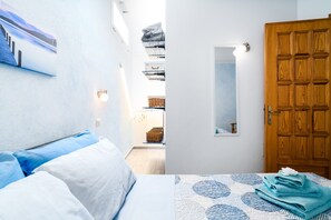 Une chambre d’hôtel avec un lit, une étagère fixée au mur où sont pliés des vêtements, une porte en bois et un petit miroir.
