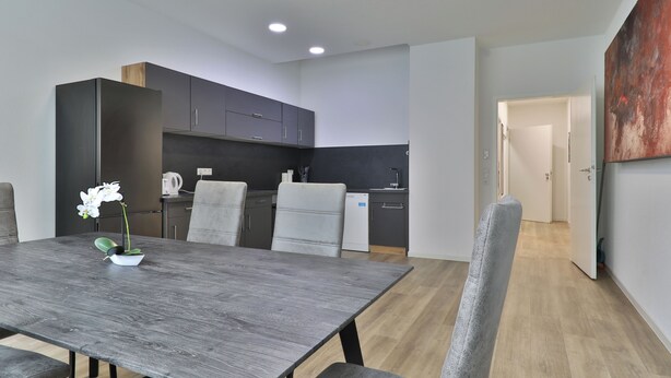 A modern kitchen with dark cabinets, a dining table with chairs, and a potted orchid. - Big Family Suite with 7 beds in the center of Göppingen (Göppingen)