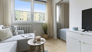 Un salon moderne avec un canapé, une petite table ronde sur laquelle est posée une bougie, une plante en pot et un téléviseur placé sur un meuble blanc.