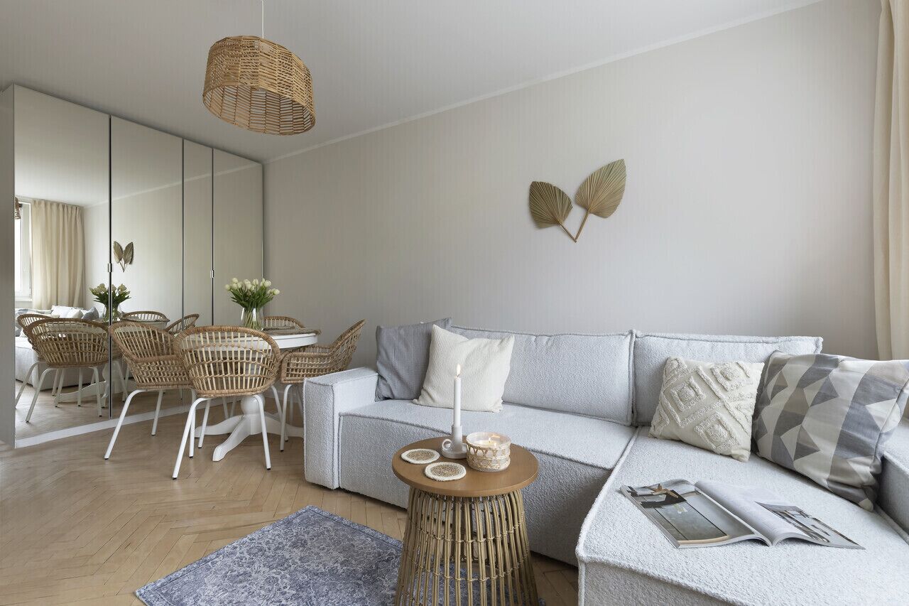 Un salon moderne avec un canapé gris, des fauteuils en osier, une petite table ronde et un grand miroir.