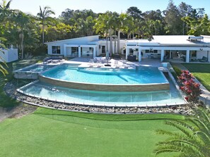 Una piscina circular grande con una terraza alrededor, un área de descanso cubierta y un césped bien cuidado.