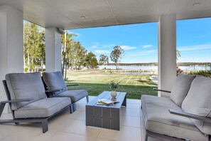 Un espacio de estar techado al aire libre con vista a un lago y paisaje cubierto de césped.