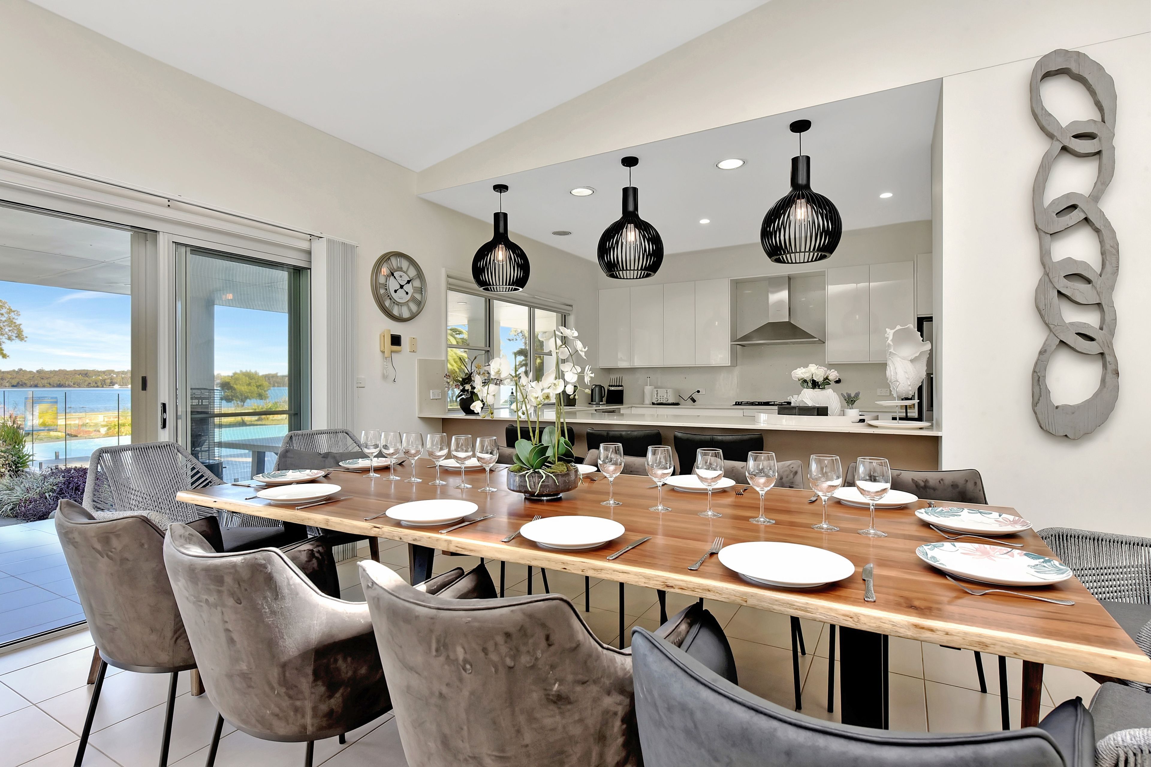 A modern dining room with a long wooden table set for a meal, surrounded by chairs.