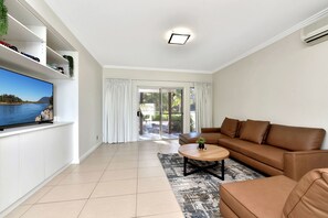 A modern living room with a flat-screen TV, a brown leather sofa, and a coffee table. - Lake Palm Resort Luxury Waterfront on 3 acres (Dora Creek)