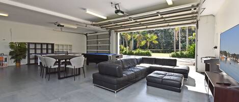 Un espacio interior amplio con mesa de billar, un sofá de cuero negro y una mesa de comedor con sillas.
