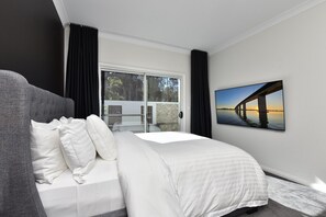 A modern bedroom with a large bed, a view of a sunset over water, and a balcony with a glass door.