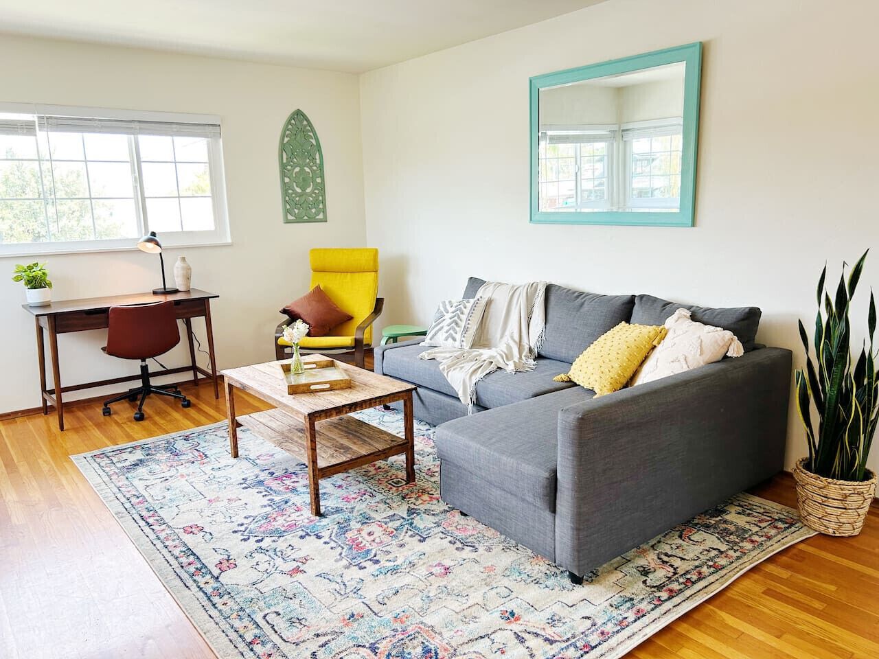 A living room with a grey sofa, a wooden coffee table, a yellow armchair, and a patterned rug.