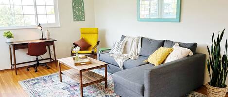 A living room with a grey sofa, a wooden coffee table, a yellow armchair, and a patterned rug.