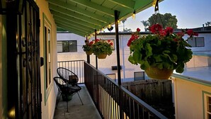 A balcony with hanging flower pots, a chair, and a railing.