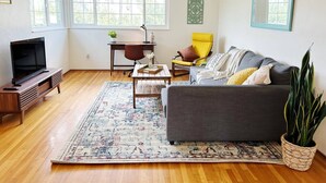 A living room with a sofa, a coffee table, a TV stand, a chair, a rug, and a potted plant.