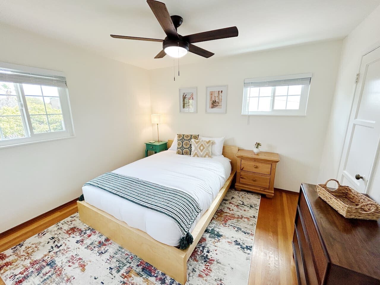A bedroom with a bed, a ceiling fan, a nightstand, a dresser, and a window.