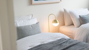 A neatly made bed with white and gray bedding, a gold-colored floor lamp, and a framed picture on the wall.