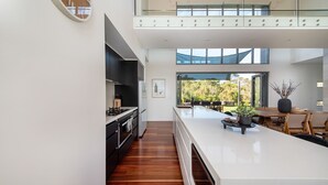 A modern kitchen with a central island, a dining area with a view, and a large window overlooking greenery.