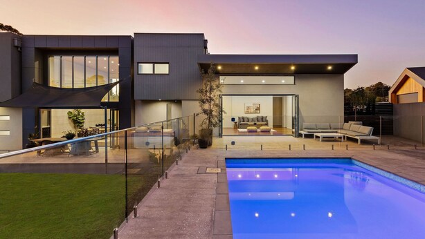A modern two-story house with a swimming pool, outdoor seating, and a glass railing.