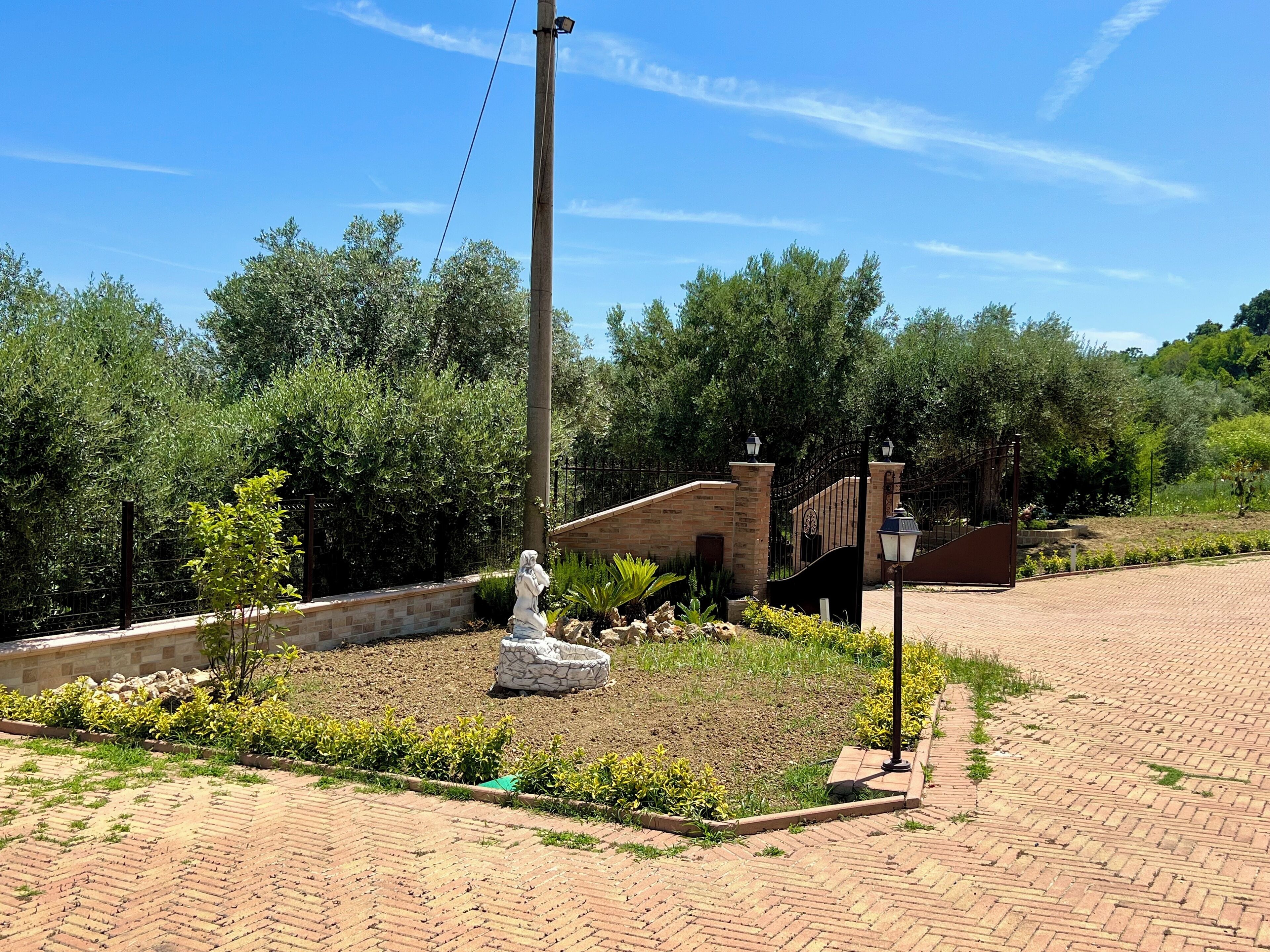 A paved area with a statue, a brick building, and a metal gate.