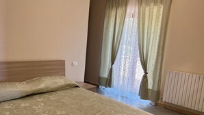 Een slaapkamer met een bed, een raam met gordijnen, een radiator en een lichtschakelaar op de muur.