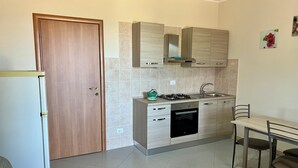Een kleine keuken met een houten deur, een gasfornuis, een spoelbak en een eethoek met een tafel en stoelen.
