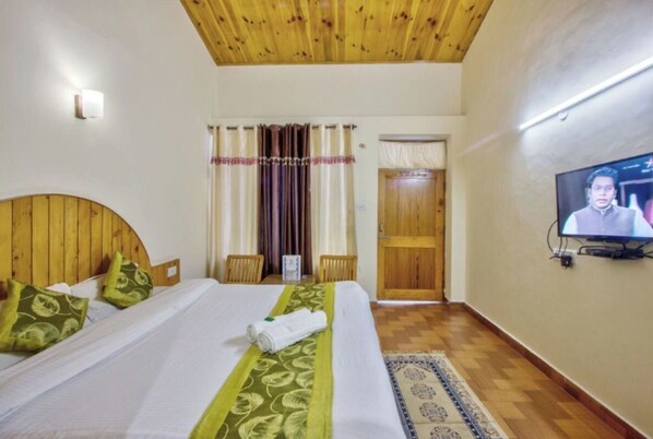 A hotel room with a wooden ceiling, a bed with green and white bedding, a television on the wall, and a wooden door. - Hotel Thakur (Manali)