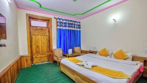 A hotel room with a wooden bed, green carpet, a wooden door, and blue curtains. - Hotel Thakur (Manali)