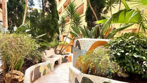 A mosaic-tiled pathway leading to a building with a pool area, surrounded by various plants and trees. - ACV - Torremar-2ª Linea Planta 1 Norte 3H (OROPESA)