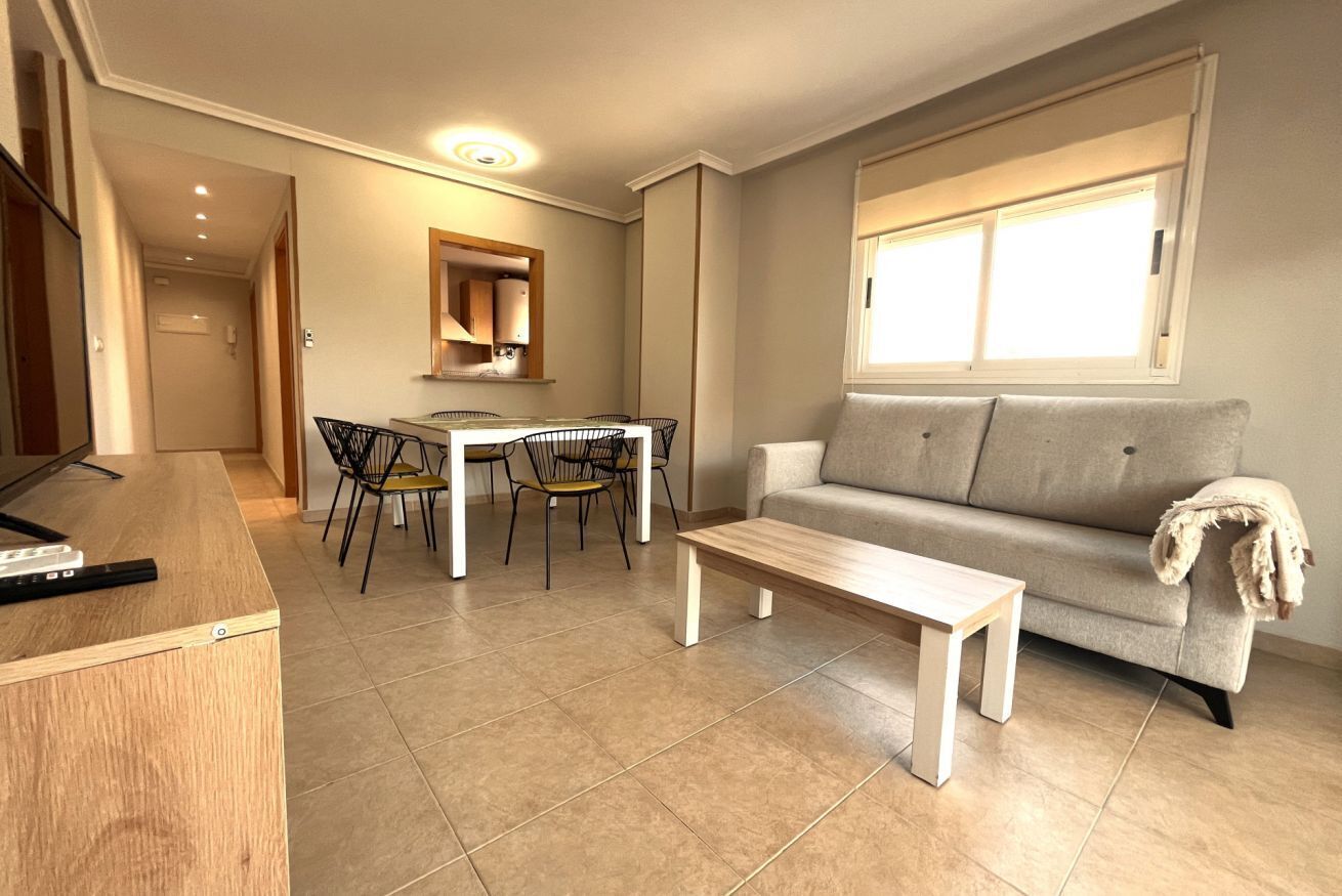 Een moderne woonkamer met een bank, een salontafel, een eettafel met stoelen en een keuken met kasten.