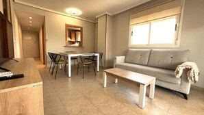A modern living room with a sofa, a coffee table, a dining table with chairs, and a kitchen area with cabinets. - ACV - Torremar-2ª Linea Planta 1 Norte 3H (OROPESA)
