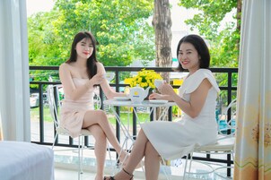 Dos mujeres sentadas en una mesa al aire libre con vista a follaje y un árbol.
