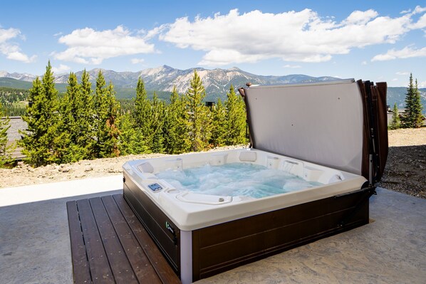 Relax on the outdoor deck with a hot tub overlooking the mountainous landscape.